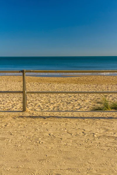 Beach with golden sand and blue sky with fence, portrait — Stock Photo, Image