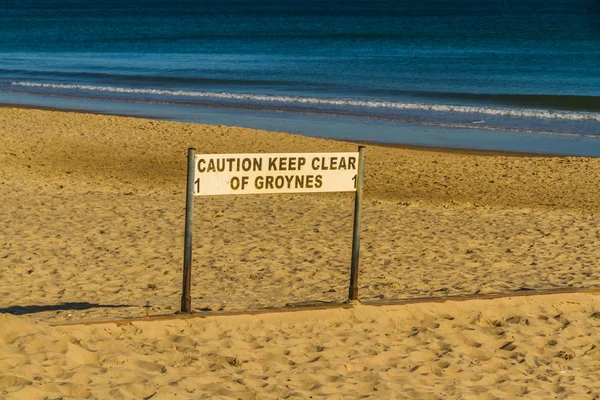 Beach with sign caution keep clear of groynes. — Stock Photo, Image
