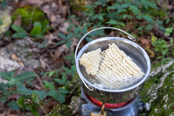 Noodles cooking in an outdoor camp stove outdoors.