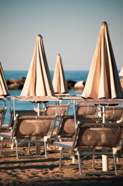 Plaj şemsiyeleri ve güneş yatakları yumuşak, eğri büğrü öğleden sonra ışığında, gün batımından önce. Riviera Romagnola bölgesinde İtalyan Adriyatik kıyıları. Eski tarz görünüş ve his. Deniz manzaralı.
