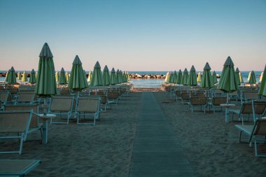 Plaj şemsiyeleri ve güneş yatakları yumuşak, eğri büğrü öğleden sonra ışığında, gün batımından önce. Riviera Romagnola bölgesinde İtalyan Adriyatik kıyıları. Eski tarz görünüş ve his. Deniz manzaralı.