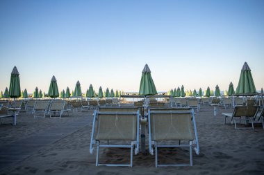 Plaj şemsiyeleri ve güneş yatakları yumuşak, eğri büğrü öğleden sonra ışığında, gün batımından önce. Riviera Romagnola bölgesinde İtalyan Adriyatik kıyıları. Eski tarz görünüş ve his. Deniz manzaralı.