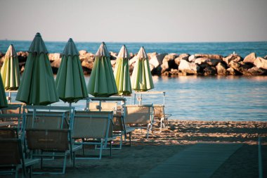 Plaj şemsiyeleri ve güneş yatakları yumuşak, eğri büğrü öğleden sonra ışığında, gün batımından önce. Riviera Romagnola bölgesinde İtalyan Adriyatik kıyıları. Eski tarz görünüş ve his. Deniz manzaralı.