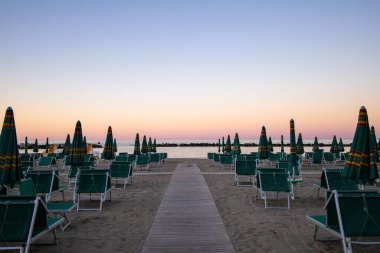 Plaj şemsiyeleri ve güneşli yataklar gün batımında mavi saatte, güzel pembe gökyüzü. Riviera Romagnola bölgesinde İtalyan Adriyatik kıyıları. Eski tarz görünüş ve his. Deniz manzarası, sihirli atmosfer.