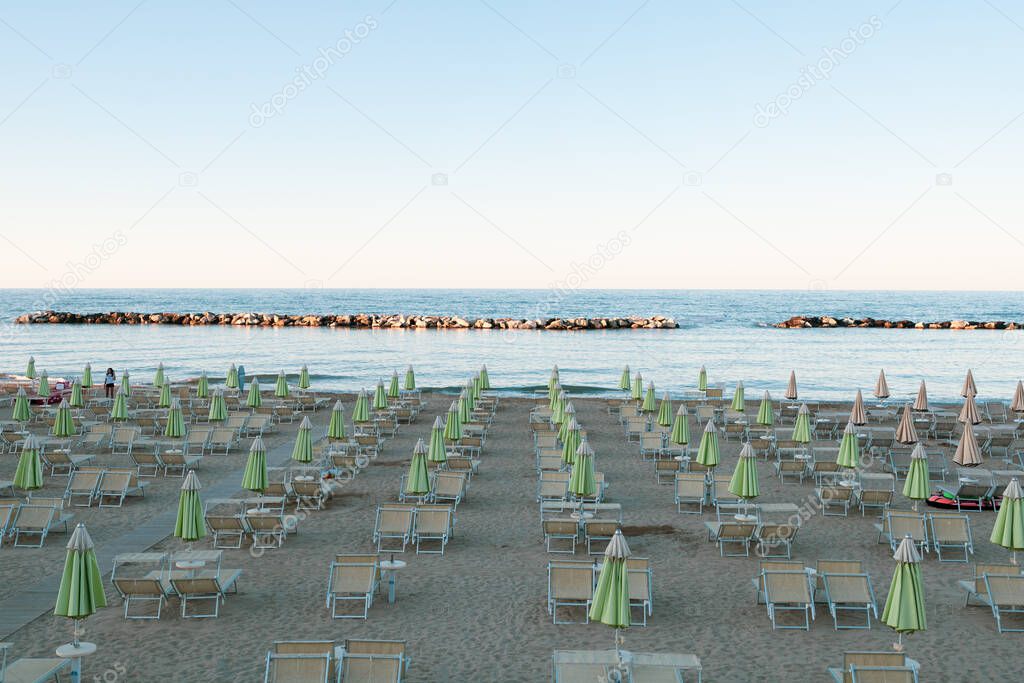 Bellaria Igea Marina, Italy, 5 july 2020 / Beach umbrellas and sunbeds in the soft light, before sunset. Italian adriatic coast in the Riviera Romagnola Area. Vintage look and feel. Sea view.
