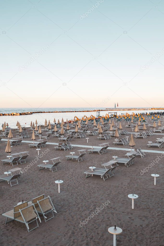 Beach umbrellas and sunbeds in the soft, oblique late afternoon light, before sunset. Italian adriatic coast in the Riviera Romagnola Area. Vintage look and feel. Sea view.