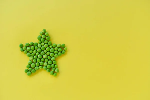 Grüne Erbsen in Form eines Sterns auf gelbem Hintergrund — Stockfoto