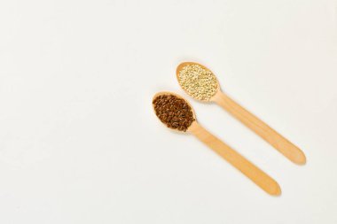 Beyaz arka planda tahta kaşıklarda keten ve susam.