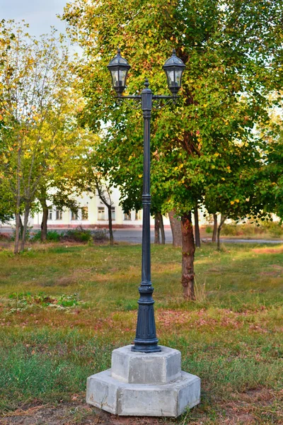 Lanterna vintage no parque de outono. Paisagem do parque de outono - árvores de outono multicoloridas laranja e uma lanterna de metal no fundo de folhas de outono amareladas no parque . — Fotografia de Stock