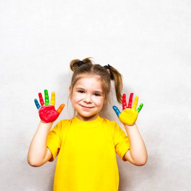 Beautiful little girl with hands in paint smiles in a yellow T-shirt. Childrens creativity.