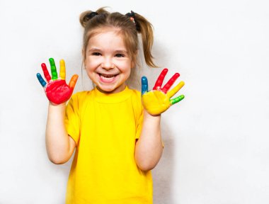 Beautiful little girl with hands in paint smiles in a yellow T-shirt. Childrens creativity.