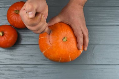 Erkek eller, gri ahşap bir masada balkabağını kesiyor. Cadılar Bayramı konsepti.
