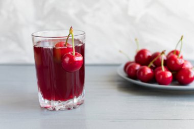 Cam bardakta kiraz suyu ve gri bir masada kiraz meyvesi. Seçici odak.