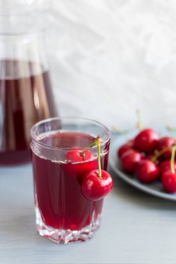 Cam bardakta kiraz suyu ve gri bir masada kiraz meyvesi. Seçici odak.