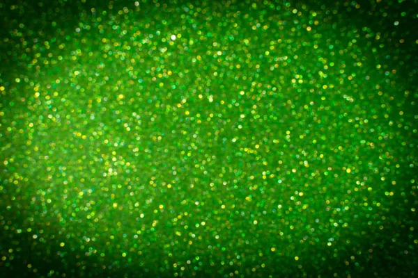 Glamor green sparkling background with dark vignette. Blured glitter background. Holiday abstract texture. Background of blue lights.