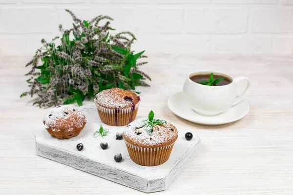 Cupcakes with black currant and mint leaves on a white plate. Selective focus. — Stock Photo, Image
