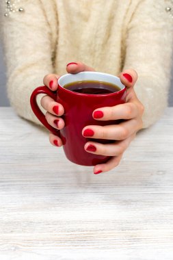 Kadın elleri kırmızı bardağı, güzel bir kızıl kış manikürlü beyaz kabarık bir kazağın arka planında tutuyor. İçki, moda, sabah. Yeni yıl. Kutlama. Çay kahve..