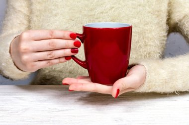 Kadın elleri kırmızı bardağı, güzel bir kızıl kış manikürlü beyaz kabarık bir kazağın arka planında tutuyor. İçki, moda, sabah. Yeni yıl. Kutlama. Çay kahve..