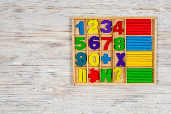 Multicolored numbers and counting sticks for studying the account in a box on a wooden white background. Concept: back to school, mathematics, arithmetic, learning to count.