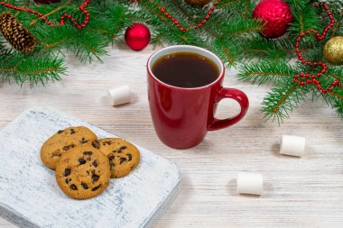 Kırmızı fincanlı çay, kurabiyeli kahve ve beyaz ahşap bir masada marshmallowlu Noel süslemeli yeni yıl ağacının arka planına karşı. Sıcaklık ve Yeni Yıl konsepti.