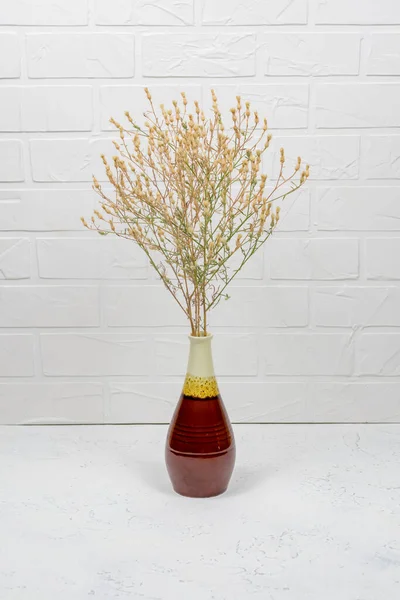 A bouquet of dry spikelets in a brown ceramic vase on a wooden table against a white brick background. Stylish home decor. Modern interior design — Stock Photo, Image