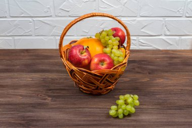 Elmalar, üzümler, balkabağı ahşap bir masanın üstünde beyaz tuğla bir duvarın arkasında..