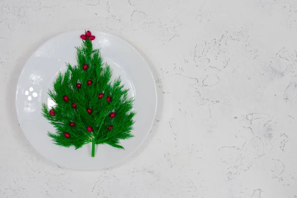 Boże Narodzenie, zima, koncepcja nowego roku - biały talerz, na którym koperek ozdobiony czerwonymi jagodami granatu. — Zdjęcie stockowe