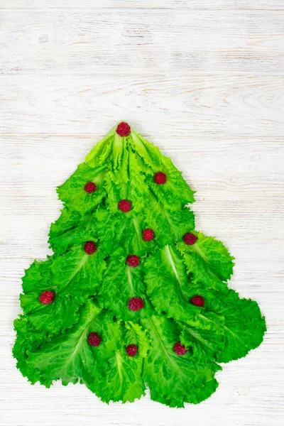 A árvore de Natal é forrada com folhas de alface verde, decoradas com framboesas vermelhas em um fundo de madeira branca. Comida para o Ano Novo. Decoração de mesa. — Fotografia de Stock