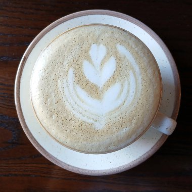 Seramik bardakta servis edilen, yaprak şeklinde köpük sanatı ile yakın plan bir latte.