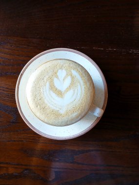 Bir bardak köpüklü kapuçino ve ahşap bir yüzey üzerinde zarif latte sanatı.