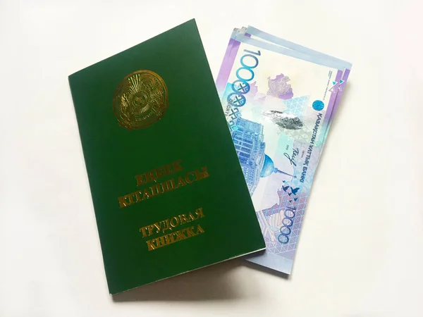 Kazakhstan employment record book with several banknotes of 10,000 Kazakhstani tenge invested in it. Closeup on white background.