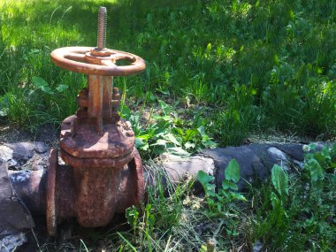 Su ile boru üzerinde eski paslı metal vana. Yeşil çimenlerde su ile eski borular.