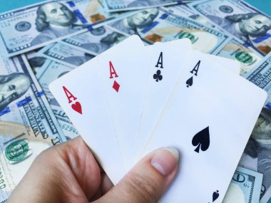 Yüz dolarlık banknotların arka planına karşı farklı takım elbiseli eski oyun kartlarının dört as kazanan bir poker eli. Üst görünüm, yakın çekim.