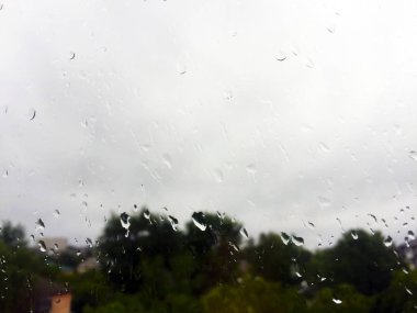 Yağmurdan bardaktan damlalar. Pencerenin dışındaki bulutlar ve yeşil ağaçlar.