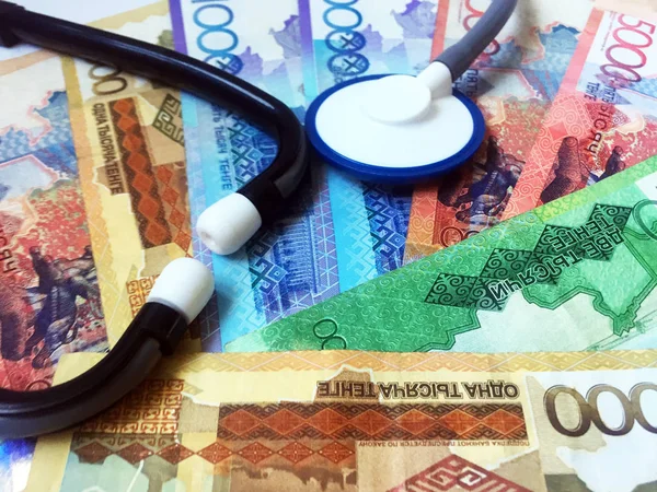 A stethoscope against a background of banknotes in denominations of 1,000, 2,000, 5,000 and 10,000 Kazakh tenge. Health care. View from above. Close-up.