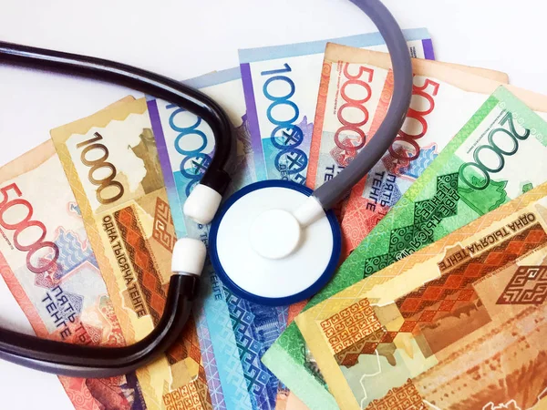 A stethoscope against a background of banknotes in denominations of 1,000, 2,000, 5,000 and 10,000 Kazakh tenge. Health care. View from above. Close-up.