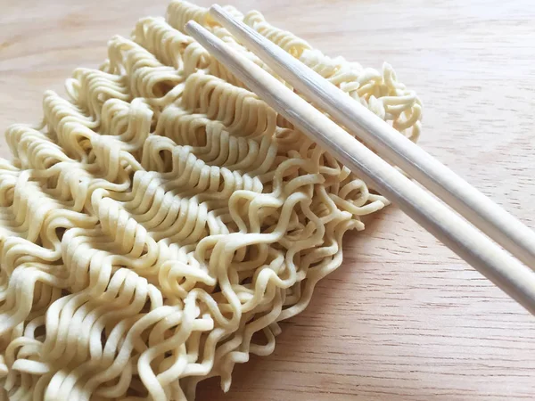 Dry thin chinese instant noodles and wooden chopsticks on a wooden table. Close-up, top view.