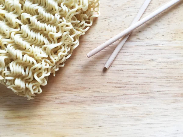 Dry thin chinese instant noodles and wooden chopsticks on a wooden table. Close-up, top view.