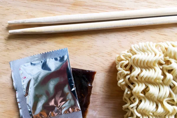 Dry thin Chinese instant noodles, wooden chopsticks and small packages with seasoning on a wooden table. Close-up, top view.