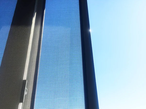 Mosquito net near the open window. White PVC plastic. Blue sky outside the window.