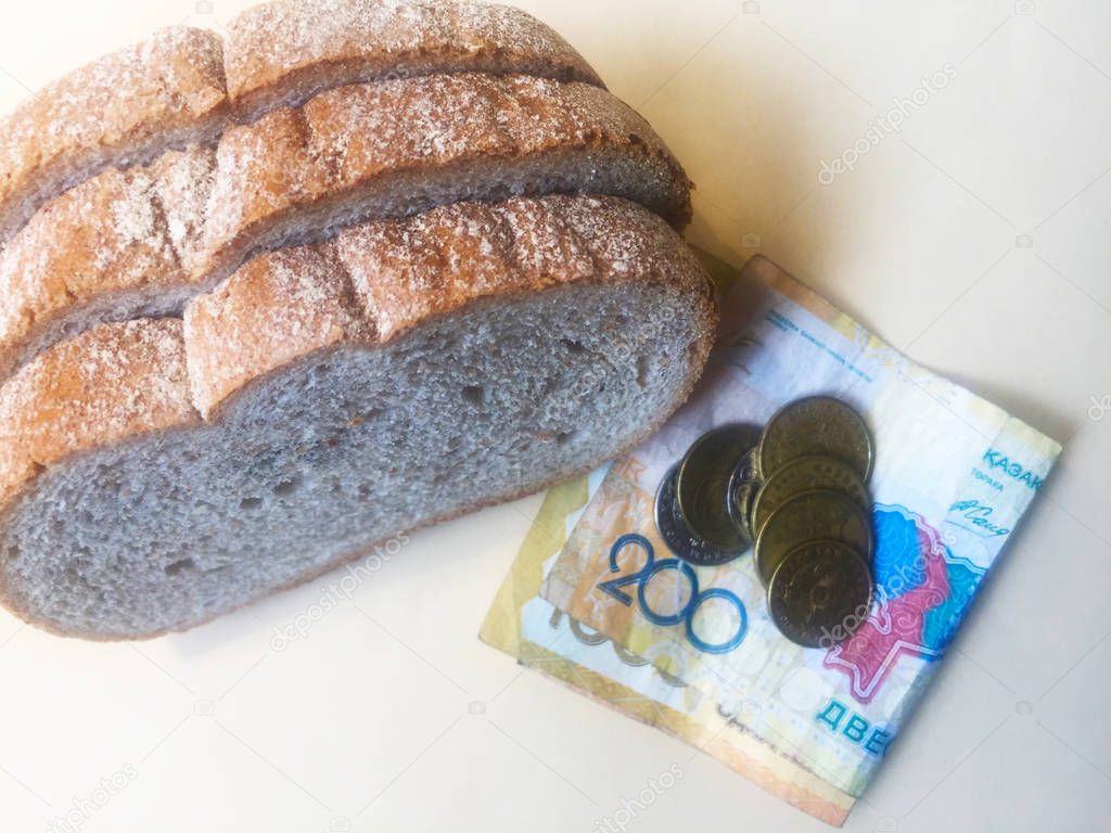 Sliced pieces of old spoiled bread and money. Banknotes of 200, 1000 Kazakhstani tenge and various coins. Close-up.