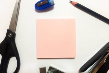 Beyaz bir arka plan üzerinde pembe çıkartmalar, siyah makas, siyah zımba, metal zımba, mavi bileyici ve siyah kalem ile Blok. Ofis kırtasiye. Yakın çekim, üst görünüm. Kopyalama alanı.