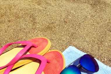 Havlu, parlak kadın plaj ayakkabıları, kum üzerinde arduvaz ve güneş gözlüğü. Kumlu sahil. Close. Metin için bir yer var.