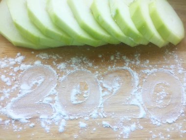 Olgun kabak parçalara ayrılmış ahşap bir masa üzerinde yatıyor. Ahşap masa un serpilir. Un üzerine yazıt 2020, yeni yıl kavramı. Close. Arka plan ve doku.