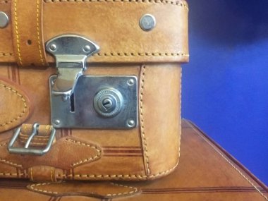 Metal kilitli kahverengi eski deriden yapılmış eski bir bavulun köşesi. Mavi duvarın yanındaki masada vintage bir bavul. Close.