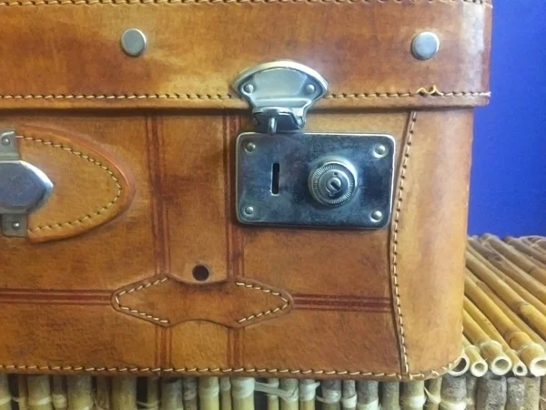 Metal kilitli kahverengi eski deriden yapılmış eski bir bavulun köşesi. Mavi duvarın yanındaki masada vintage bir bavul. Close.