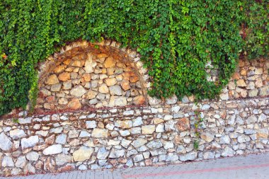 Taş duvardaki sarmaşık. Duvar farklı boyutlarda ve kemerler ile şekillerde doğal taştan yapılmış bir parçası, yeşil bitkiler ile dolaşık. Eski taş bina boyunca yol. Yakın çekim, güzel arka plan
