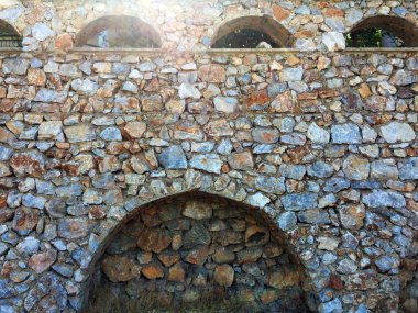 Farklı ebat ve şekillerde doğal taştan yapılmış girinti ler ve kemerler ile duvarın bir parçası. Eski taş bina boyunca yol. Yakın çekim, güzel arka plan ve ilginç doku.