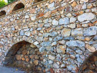 Farklı ebat ve şekillerde doğal taştan yapılmış girinti ler ve kemerler ile duvarın bir parçası. Eski taş bina boyunca yol. Yakın çekim, güzel arka plan ve ilginç doku.