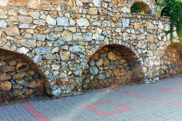 Farklı ebat ve şekillerde doğal taştan yapılmış girinti ler ve kemerler ile duvarın bir parçası. Eski taş bina boyunca yol. Yakın çekim, güzel arka plan ve ilginç doku.